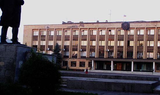 Здание районной и городской администрации на закате. Над входом в здание виден бронзовый герб РСФСР, а слева — статуя Ленина.